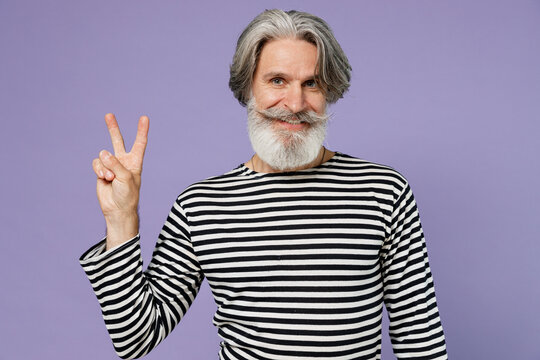 Elderly smiling happy gray-haired mustache bearded man 50s wearing striped turtleneck showing victory sign isolated on plain pastel light purple background studio portrait. People lifestyle concept.