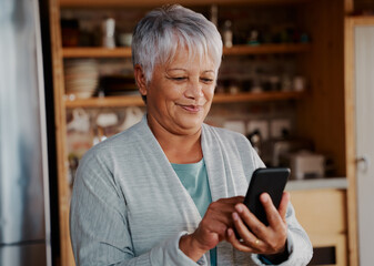 Smiling multi-cultural elderly female scrolling internet on smartphone while standing in modern...