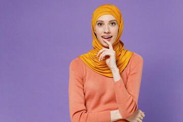 Smart surprised young arabian asian muslim woman in abaya hijab yellow clothes holding index finger near chin as find great new idea isolated on plain pastel light violet background studio portrait. - obrazy, fototapety, plakaty