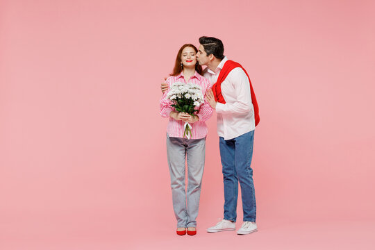 Full Body Young Couple Two Friends Woman Man 20s In Shirt Give Bouquet Of Flowers Kiss Cheek Isolated On Plain Pastel Pink Background Studio Portrait. Valentine's Day Birthday Holiday Party Concept.