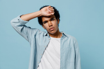 Sick young black curly man 20s years old wear white shirt put hands on head rub temples having headache suffering from migraine feel bad isolated on plain pastel light blue background studio portrait