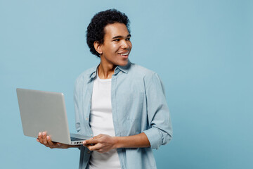 Fascinating excited delight young black curly man 20s years old wear white shirt hold use work on laptop pc computer looking back behind isolated on plain pastel light blue background studio portrait