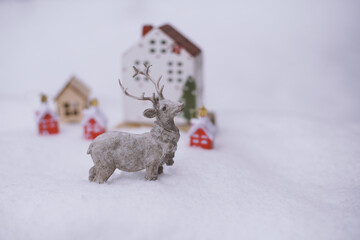 The figure of a deer, toy houses, fir branches in the snow.