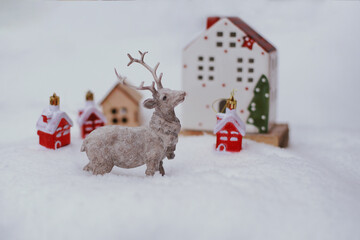 The figure of a deer, toy houses, fir branches in the snow.
