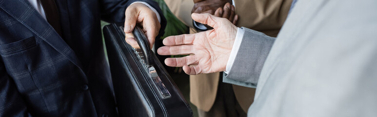 partial view of senior man holding briefcase near interracial business partners, banner
