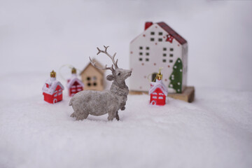 The figure of a deer, toy houses, fir branches in the snow.