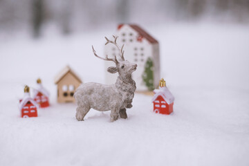 The figure of a deer, toy houses, fir branches in the snow.