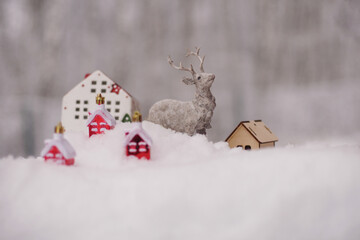 The figure of a deer, toy houses, fir branches in the snow.