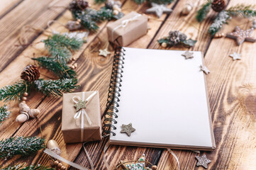 Notepad, gifts, fir branches, cones and stars lying on a wooden table top. New Year's plans. Place to insert