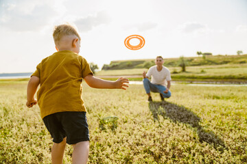 Young white father and son playing with frisbee together - obrazy, fototapety, plakaty