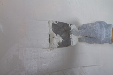 Apply plaster white putty on a concrete wall with a spatula