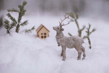 The figure of a deer, toy houses, fir branches in the snow.