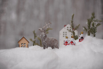 The figure of a deer, toy houses, fir branches in the snow.