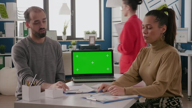Team of workers having laptop with green screen on desk. Man and woman doing teamwork and using mockup template with chroma key and isolated blank background. Chroma-key copy space
