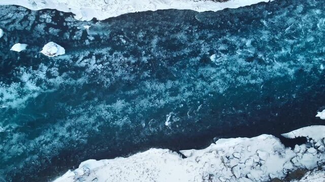Strong streams of cold blue water and melting ice from waterfall. Natural pattern ice water and foam in the north of Iceland.