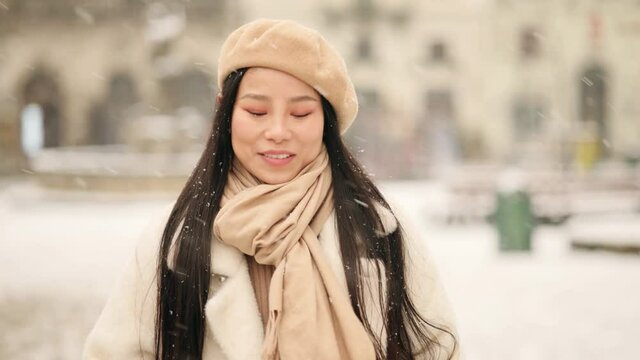 Portrait of young beautiful asian woman walking down and looking at the camera at the snowy city centre. Close up of happy young girl smiling. High quality 4k footage