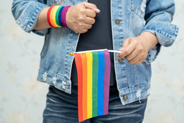 Asian lady wearing blue jean jacket or denim shirt and holding rainbow color flag, symbol of LGBT...