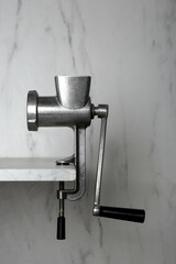 Metal manual meat grinder on table against white marble background