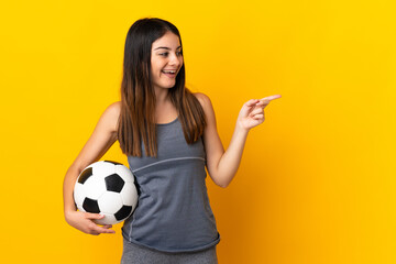 Young football player woman isolated on yellow background pointing finger to the side and presenting a product