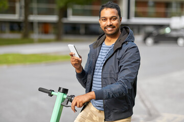 transport, technology and people and concept - happy smiling young man with electric scooter using smartphone on city street