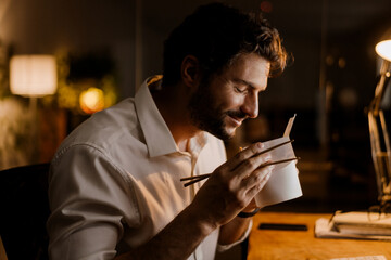 White man eating asian noodles and smiling while working in office