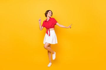 Fototapeta na wymiar Full size photo of charming positive lady look empty space point fingers enjoy dancing isolated on yellow color background