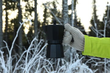Hand in mitten holds coffee maker in forest