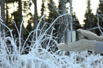 Hands in mittens hold metal cup in forest