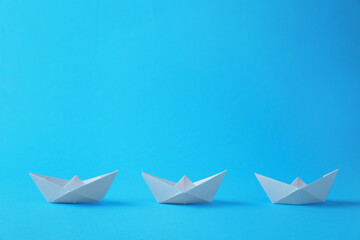 Handmade white paper boats on light blue background. Origami art