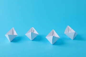 Handmade white paper boats on light blue background. Origami art