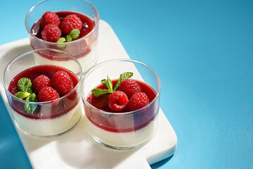 Italian dairy dessert panna cotta with raspberry jam and fresh raspberries on marble board on blue surface, negative space