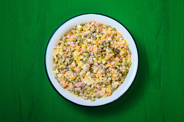 traditional festive dish of Russian cuisine - olivier salad in a large white bowl on a green background