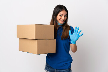 Young delivery woman protecting from the coronavirus with a mask isolated on white background saluting with hand with happy expression