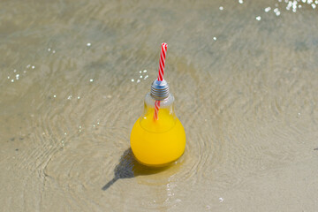 Fresh, lemonade or cocktail in a glass bottle with a straw close-up on the beach sand near the water. Travel and recreation concept.
