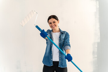 Positive overjoyed woman holding and stretching to the camera dirty roller after painting walls in room. People renovation and home improvement concept