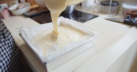 woman pouring homemade fresh raw batter cream into baking Form box pan for baking bakery cake at...