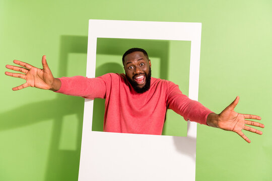Portrait of overjoyed handsome man raise arms through photo card frame isolated on green color background