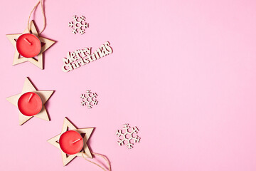 Fototapeta na wymiar Christmas composition of wooden stars, red candles and snowflakes on pink paper background with copy space