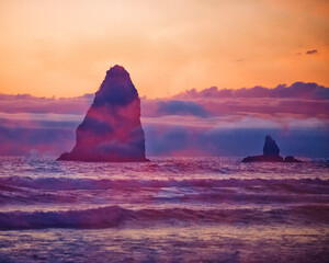 Islands of rock arise from the water and waves of the shoreline of Cannon Beach, Oregon during a golden sunset.