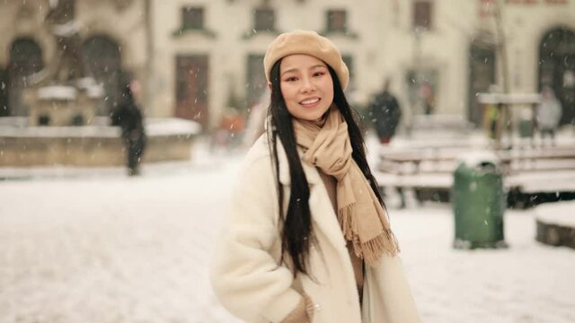 Portrait of young beautiful asian woman walking down and looking at the camera at the snowy city centre. Close up of happy young girl smiling. High quality 4k footage