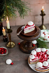 Sponge mousse cake with cranberry jam and decorated with meringues. Festive cake for the New Year's table with candles and pine branches.