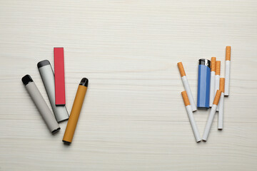Cigarettes with lighter and different vaping devices on white wooden background, flat lay. Smoking...