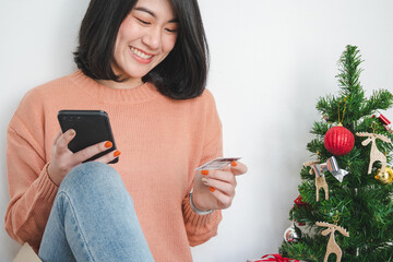 young woman sit on floor, using mobile phone, and holding credit card for christmas online shopping