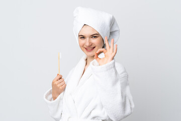 Young woman in a bathrobe holding toothbrush showing ok sign with fingers