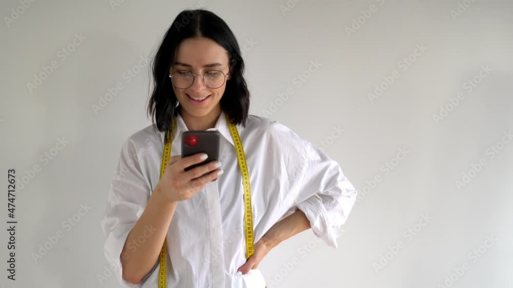 Poster young smiling female reading text message on smartphone while standing front blank copy space wall. 