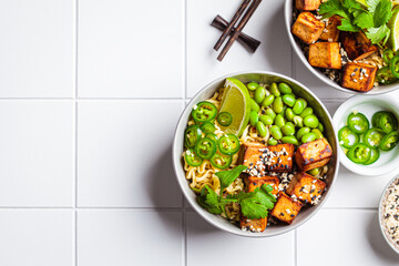 Vegan noodles ramen soup with marinated tofu, edamame beans and hot peppers in gray bowls.