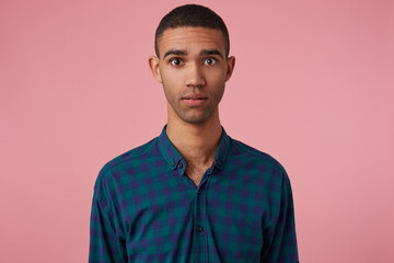 studio portrait of middle age middle eastern man wears blue checkered shirt starring into camera with emotionless facial expression, feels calm. isolated over pink background