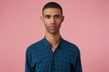studio portrait of middle age middle eastern man wears blue checkered shirt starring into camera with emotionless facial expression, feels calm. isolated over pink background
