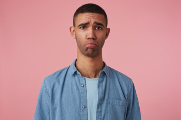 studio portrait of middle age middle eastern man wears blue shirt looks into camera with sad facial expression, curving his lip isolated over pink background