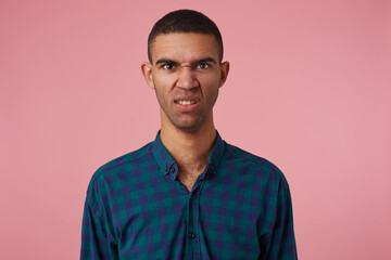Obraz premium studio portrait of middle age middle eastern man wears blue checkered shirt grin with angry facial expression. isolated over pink background